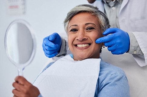 Patient smiling while holding handheld mirror in treatment room