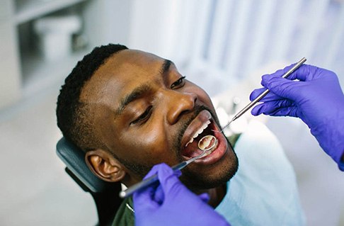 Dentist with blue gloves examining patient's teeth