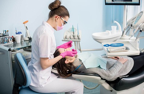 Dental hygienist cleaning patient's teeth in treatment room