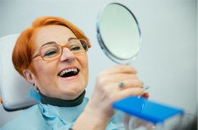 A mature woman admiring her dentures in a hand mirror