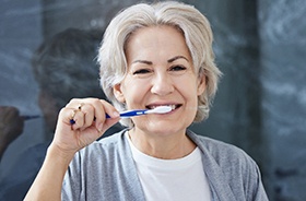 A woman brushing her teeth after dental implant surgery