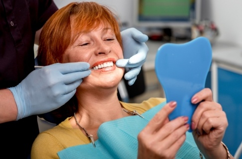 Woman looking at smile after tooth replacement with dental implants