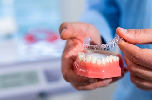 Dentist placing clear aligner on model of teeth