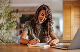 Woman smiling while taking notes at desk
