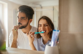 Couple smiling while brushing their teeth in bathroom