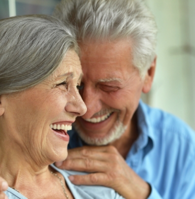 Older man and woman smiling after replacing missing teeth